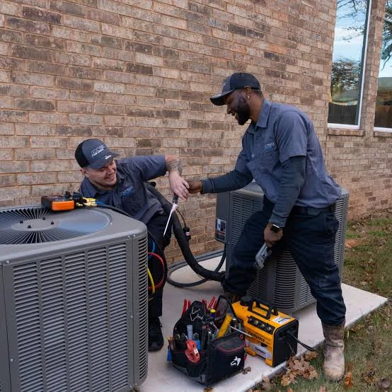 Two HVAC technicians working together on residential air conditioning equipment