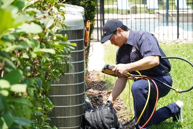 HVAC technician performing outdoor air conditioner maintenance beside a home